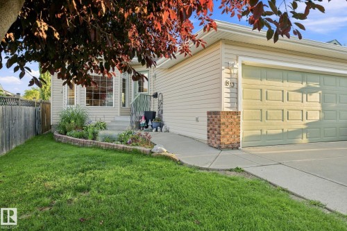 Front exterior featuring light-toned siding, a bay window, an attached garage, a concrete driveway, and a fenced side yard - 30 Belfry Fairway Crescent, Stony Plain, AB 