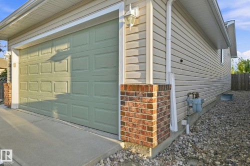 Light green paneled garage door, brick column accents, beige horizontal siding, white trim, and a concrete driveway - 30 Belfry Fairway Crescent, Stony Plain, AB 