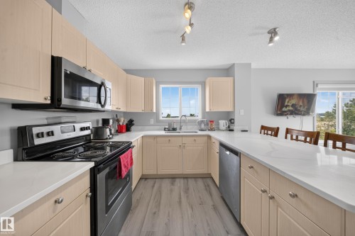 Kitchen featuring light-toned cabinetry, stainless steel appliances, white countertops, wood-finish flooring, and track lighting - #419 4407 23 St Nw, Edmonton, AB 