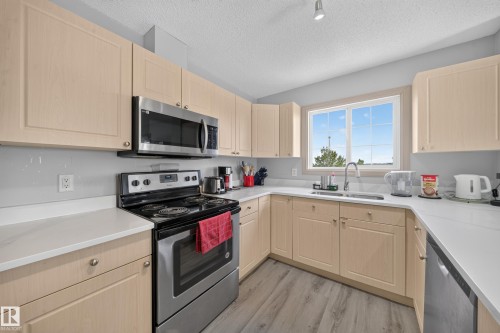 U-shaped kitchen featuring light wood-finish cabinetry, stainless steel appliances, white countertops, and a window above the sink - #419 4407 23 St Nw, Edmonton, AB 