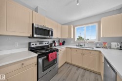 U-shaped kitchen featuring light wood-finish cabinetry, stainless steel appliances, white countertops, and a window above the sink - 