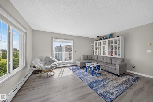 Spacious living area featuring light gray walls, wood-finish flooring, and large windows - #419 4407 23 St Nw, Edmonton, AB 