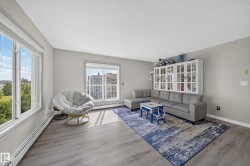 Spacious living area featuring light gray walls, wood-finish flooring, and large windows - 