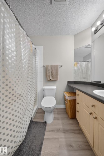Wood-finish flooring, light tone cabinetry with decorative hardware, solid surface countertop, vanity lighting, and a built-in mirror - #419 4407 23 St Nw, Edmonton, AB 