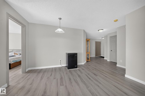 Open-concept living space featuring gleaming wood-finish flooring throughout, white painted walls, and abundant natural light from multiple windows - #419 4407 23 St Nw, Edmonton, AB 