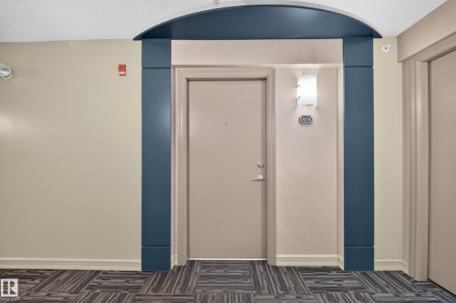 Entryway featuring a decorative arched doorway, wall sconce, and patterned carpet flooring - #419 4407 23 St Nw, Edmonton, AB 