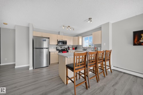 Kitchen featuring light wood-finish cabinetry, stainless steel appliances, a light-toned countertop, and wood-finish flooring - #419 4407 23 St Nw, Edmonton, AB 