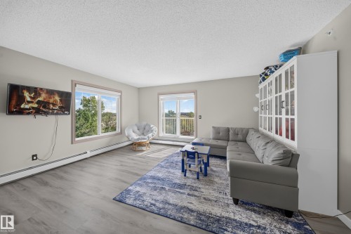 Wood-finish flooring, light grey wall paint, multiple windows, and a built-in display cabinet - #419 4407 23 St Nw, Edmonton, AB 
