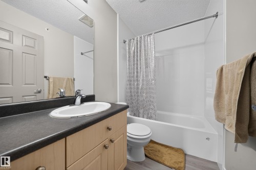 Bathroom featuring a light wood-finish vanity, dark countertop, oval undermount sink, and a white tub with shower surround - #419 4407 23 St Nw, Edmonton, AB 