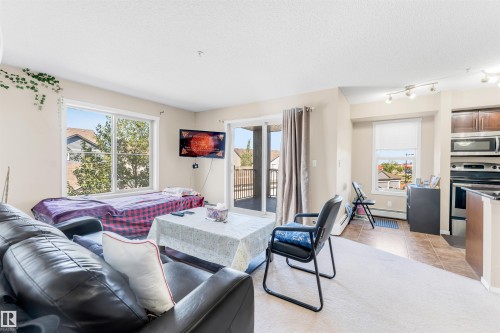 Living area featuring light-toned walls, a large window, and a sliding glass door providing access to a private balcony - #225 111 Watt Cm Sw, Edmonton, AB 