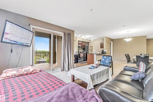 Open-concept living space with a sliding glass door to a balcony, a kitchen with dark wood-finish cabinetry, and a dining area featuring a pendant light fixture - #225 111 Watt Cm Sw, Edmonton, AB 