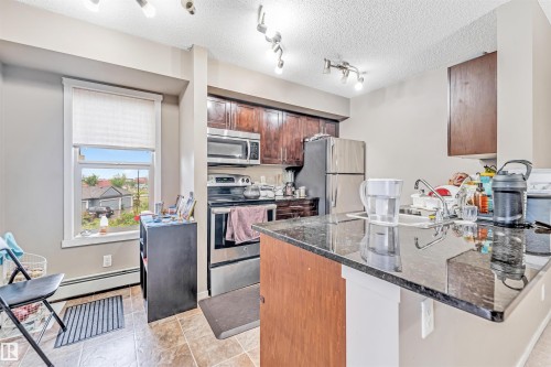 Kitchen featuring dark wood-finish cabinetry, stainless steel appliances, and a breakfast bar with a dark stone-finish countertop - #225 111 Watt Cm Sw, Edmonton, AB 