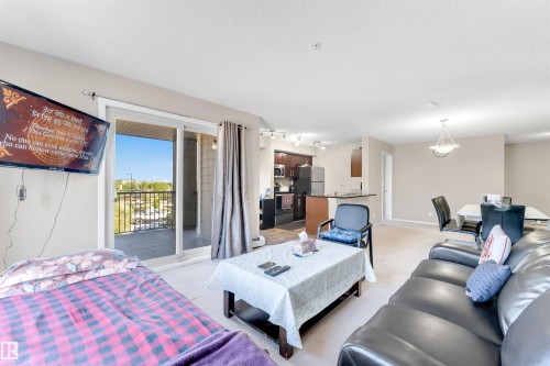 Sliding glass door leading to a private balcony, kitchen with dark wood cabinetry and black appliances, dining area with overhead lighting, and an open concept living space - #225 111 Watt Cm Sw, Edmonton, AB 
