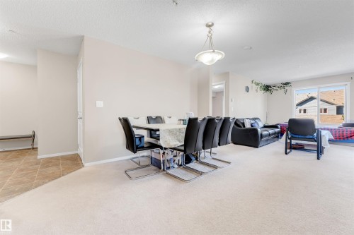 Open-concept living space with carpet flooring and a dining area featuring a hanging light fixture - #225 111 Watt Cm Sw, Edmonton, AB 