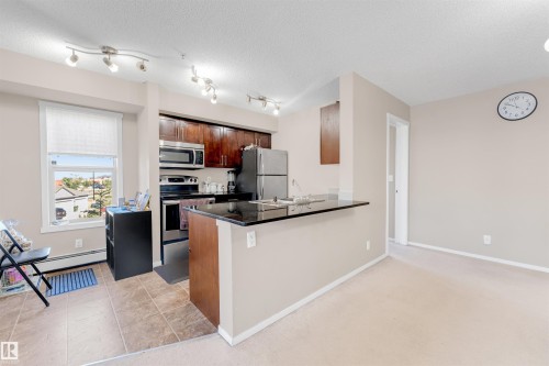 Kitchen featuring stainless steel appliances, dark wood-finish cabinetry, and a black countertop peninsula - #225 111 Watt Cm Sw, Edmonton, AB 