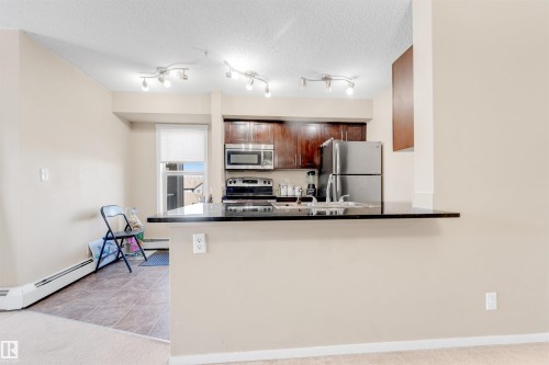 Kitchen featuring dark wood-finish cabinetry, black countertops, stainless steel appliances, and track lighting - #225 111 Watt Cm Sw, Edmonton, AB 