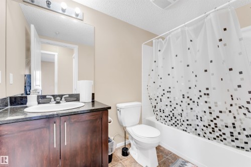 Bathroom featuring a dark wood-finish vanity, white undermount sink, dark countertop, and a white bathtub with shower - #225 111 Watt Cm Sw, Edmonton, AB 
