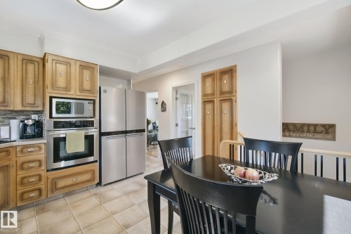Built-in microwave and oven, stainless steel refrigerator, wood cabinetry, tile flooring, and a built-in storage cabinet - 12916 63 Street Nw, Edmonton, AB 