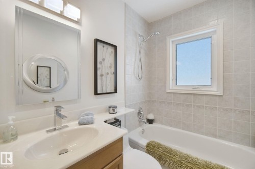 Bathroom featuring a light wood-finish vanity, polished chrome faucet, built-in bathtub, and tiled shower surround with an integrated window - 12916 63 Street Nw, Edmonton, AB 