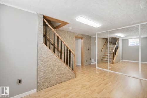 Wood-finish flooring, staircase with wood handrail and black balusters, mirrored wall, recessed window, and flush-mount ceiling lights - 12916 63 Street Nw, Edmonton, AB 