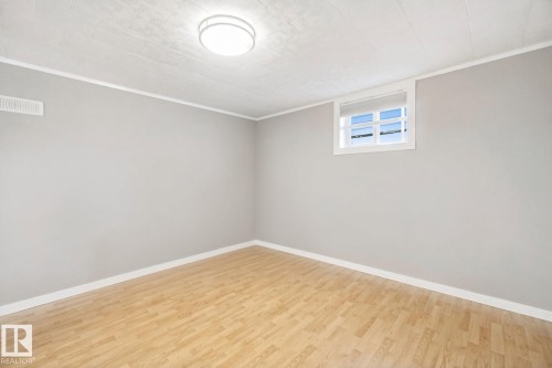 Neutral gray walls with white trim, wood-finish flooring, a white-framed window, and a flush-mount ceiling light fixture - 12916 63 Street Nw, Edmonton, AB 