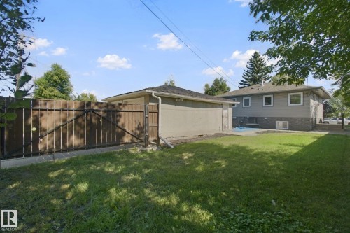 Fenced yard with a detached garage, concrete patio, and a two-story exterior featuring gray siding and a brick-look lower level - 12916 63 Street Nw, Edmonton, AB 