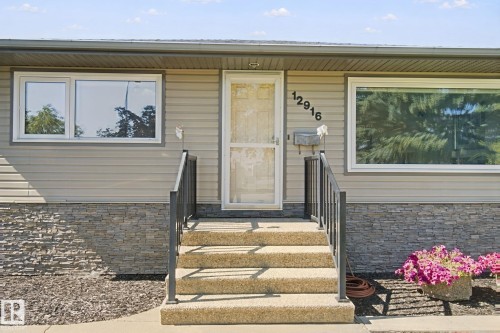 Exterior siding with stone veneer detailing, white window frames, and a white storm door - 12916 63 Street Nw, Edmonton, AB 