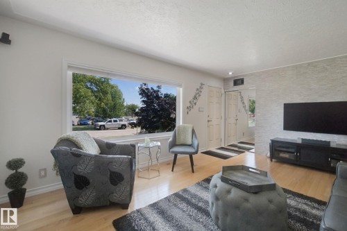 Spacious living area featuring light wood-finish flooring, a textured accent wall, and a large picture window - 12916 63 Street Nw, Edmonton, AB 