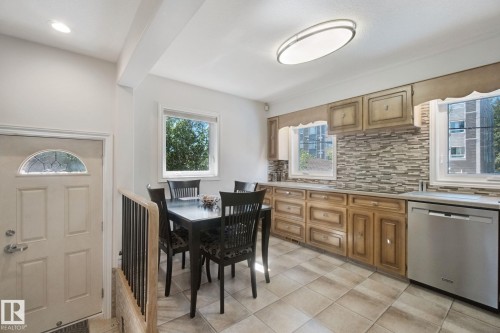 Kitchen featuring wood cabinetry, stone-look tile backsplash, stainless steel dishwasher, and tile flooring - 12916 63 Street Nw, Edmonton, AB 