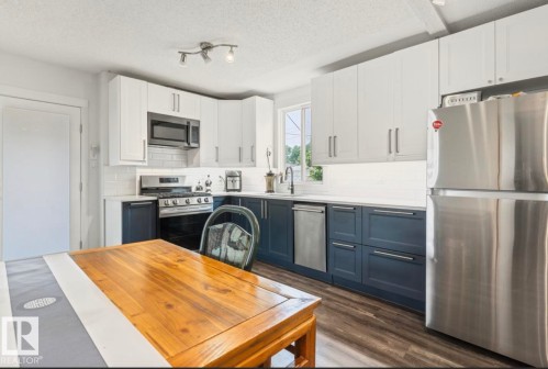 Kitchen featuring two-tone cabinetry, stainless steel appliances, a white subway tile backsplash, and wood-finish flooring - 12150 47 Street Nw, Edmonton, AB - Indoor Photo Showing Kitchen