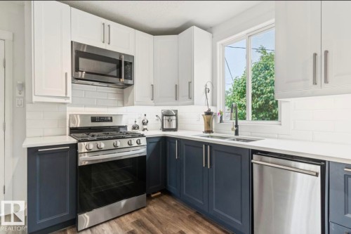 Kitchen featuring two-tone cabinetry, white subway tile backsplash, stainless steel appliances, white countertops, and wood-finish flooring - 12150 47 Street Nw, Edmonton, AB - Indoor Photo Showing Kitchen With Double Sink