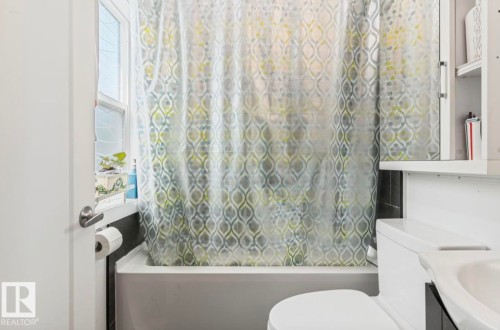 Bathroom featuring a white bathtub, a toilet with a white tank, dark wall tiling, a window, and a built-in medicine cabinet - 12150 47 Street Nw, Edmonton, AB - Indoor Photo Showing Bathroom