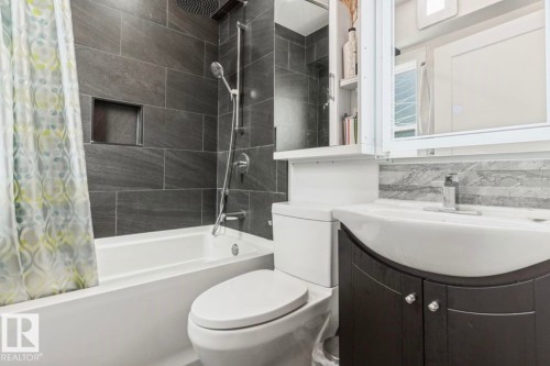 Contemporary bathroom featuring a full-size bathtub, integrated shower niche, dark gray tile surround, rainfall shower head, and a vanity with a vessel sink - 12150 47 Street Nw, Edmonton, AB - Indoor Photo Showing Bathroom