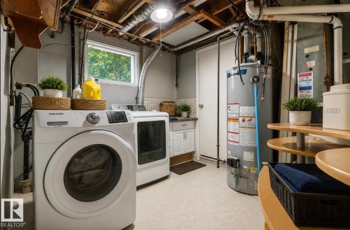 Dedicated laundry area featuring a full-size washer and dryer, a window, a single-door cabinet with a light-toned countertop, a water heater, and exposed ceiling joists - 12150 47 Street Nw, Edmonton, AB - Indoor Photo Showing Laundry Room