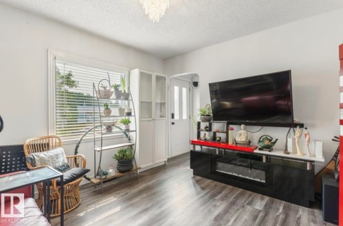 Living area with wood-finish flooring, white walls, and a large window featuring horizontal blinds - 12150 47 Street Nw, Edmonton, AB - Indoor Photo Showing Living Room