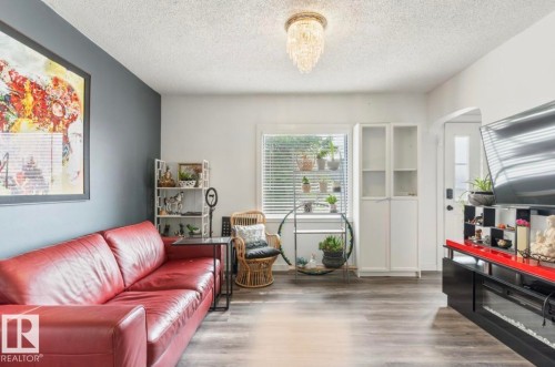 Living area featuring wood-finish flooring, a crystal chandelier, a white framed window with blinds, and a built-in white storage cabinet with glass-front doors - 12150 47 Street Nw, Edmonton, AB - Indoor Photo Showing Living Room