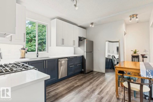 Modern kitchen featuring two-tone cabinetry, stainless steel appliances, a gas range, white subway tile backsplash, and wood-finish flooring - 12150 47 Street Nw, Edmonton, AB - Indoor Photo Showing Kitchen