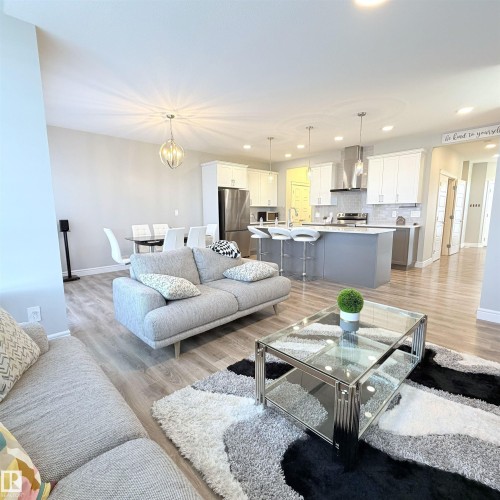 Open-concept living area with wood-finish flooring, recessed lighting, a modern chandelier, and a kitchen featuring stainless steel appliances and a center island - 1003 Goldfinch Way Nw, Edmonton, AB 
