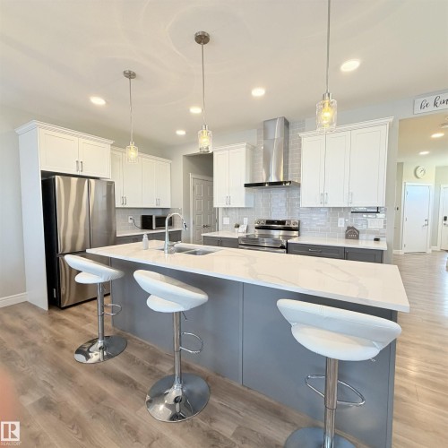 Kitchen featuring a large island with a double basin sink, white countertops, and wood-finish flooring - 1003 Goldfinch Way Nw, Edmonton, AB 
