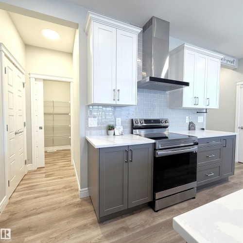 Two-tone cabinetry with crown molding, stainless steel appliances, subway tile backsplash, light wood-finish flooring, and a walk-in pantry with wire shelving - 1003 Goldfinch Way Nw, Edmonton, AB 