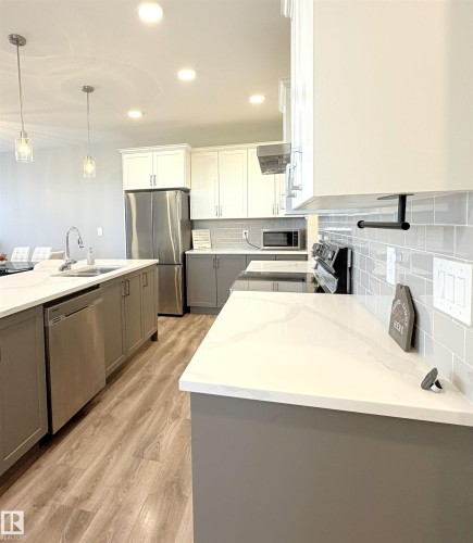 Kitchen featuring white upper cabinetry, gray lower cabinetry, light-toned wood-finish flooring, and white countertops - 1003 Goldfinch Way Nw, Edmonton, AB 