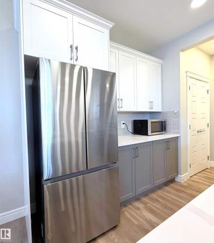 Stainless steel refrigerator, two-tone cabinetry with crown molding, light-colored countertops, subway tile backsplash, and wood-finish flooring - 1003 Goldfinch Way Nw, Edmonton, AB 