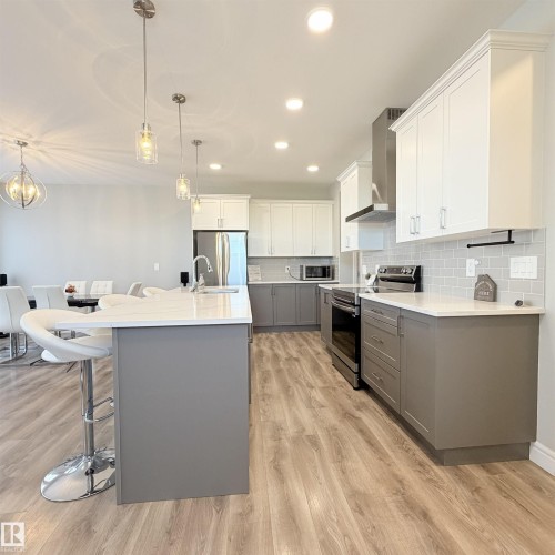 Contemporary kitchen featuring two-tone cabinetry, stainless steel appliances, a subway tile backsplash, recessed lighting, and wood-finish flooring - 1003 Goldfinch Way Nw, Edmonton, AB 
