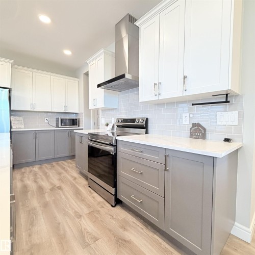 Kitchen featuring two-tone cabinetry, wood-finish flooring, white countertops, and a subway tile backsplash - 1003 Goldfinch Way Nw, Edmonton, AB 