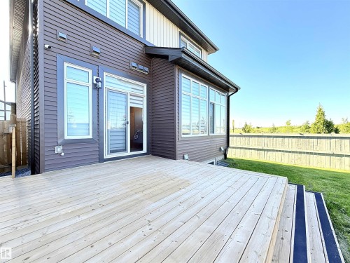 Expansive outdoor deck with steps leading to a manicured lawn, featuring brown horizontal siding, multiple large windows, and a sliding glass door - 1003 Goldfinch Way Nw, Edmonton, AB 