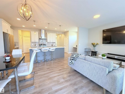 Open-concept living area with wood-finish flooring, a contemporary chandelier, recessed lighting, and a kitchen island with pendant lights - 1003 Goldfinch Way Nw, Edmonton, AB 