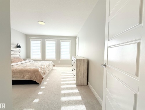 Spacious room featuring three large windows, light-toned carpeting, and a contemporary five-panel interior door - 1003 Goldfinch Way Nw, Edmonton, AB 