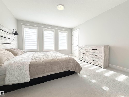 Recessed ceiling light fixture, three windows with horizontal blinds, carpeted flooring, and a six-drawer dresser with dark hardware - 1003 Goldfinch Way Nw, Edmonton, AB 