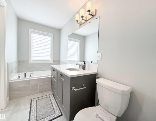 Built-in soaking tub with tile surround, a single vanity with stone countertop, and a wall-mounted mirror with integrated lighting - 1003 Goldfinch Way Nw, Edmonton, AB 