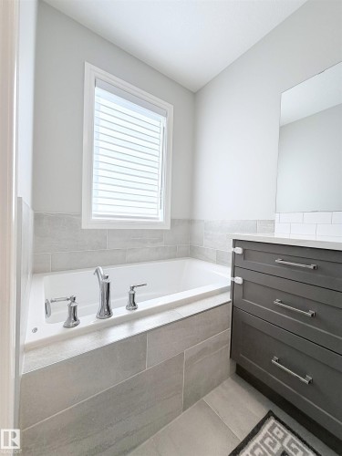 Built-in bathtub with polished chrome fixtures, surrounded by light gray large format tile - 1003 Goldfinch Way Nw, Edmonton, AB 